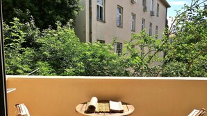 A balcony with two wooden chairs and a small round table, overlooking a building and lush greenery. - Klarina Apartments (Split)