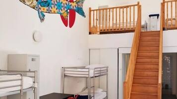 A dormitory room with bunk beds, a wooden staircase, a desk with a chair, and a colorful fish mural on the wall.