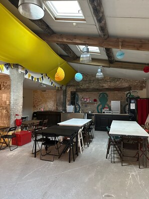 Una habitación amplia con techos altos, paredes de ladrillo visto y un tragaluz. Hay varias mesas y sillas dispuestas para cenar o reuniones.