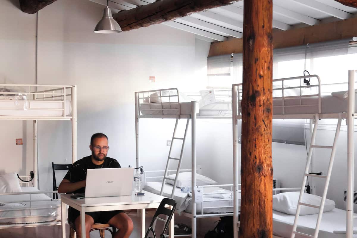 Une chambre de dortoir avec des lits superposés, un bureau avec un ordinateur portable et un pilier en bois.