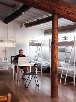 Un dormitorio con literas, un escritorio con una computadora portátil y un pilar de madera.