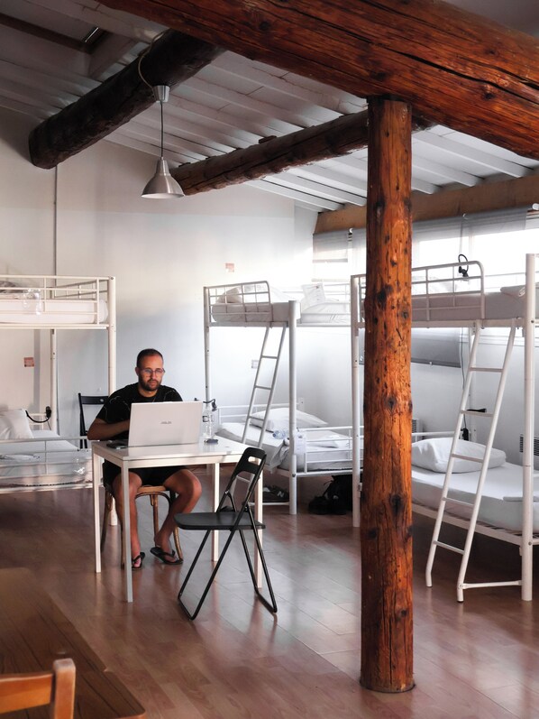 A dormitory room with bunk beds, a desk with a laptop, and a wooden pillar.