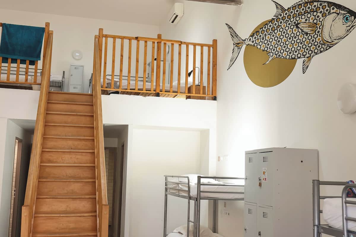 Une chambre de dortoir avec des lits superposés, un escalier en bois et une fresque représentant des poissons sur le mur.