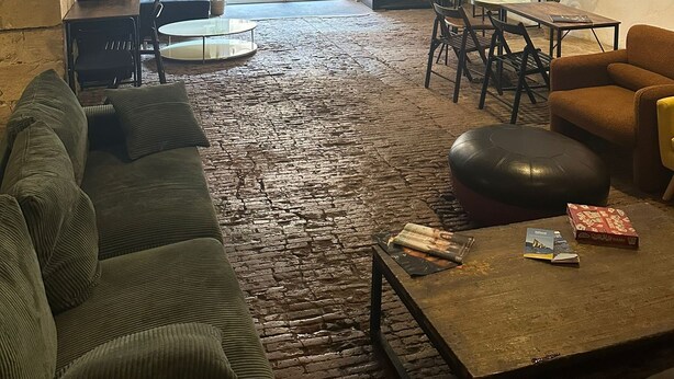 Un interior rústico con vigas de madera a la vista, piso de ladrillo y una variedad de asientos, incluyendo un sofá, sillas y una mesa.