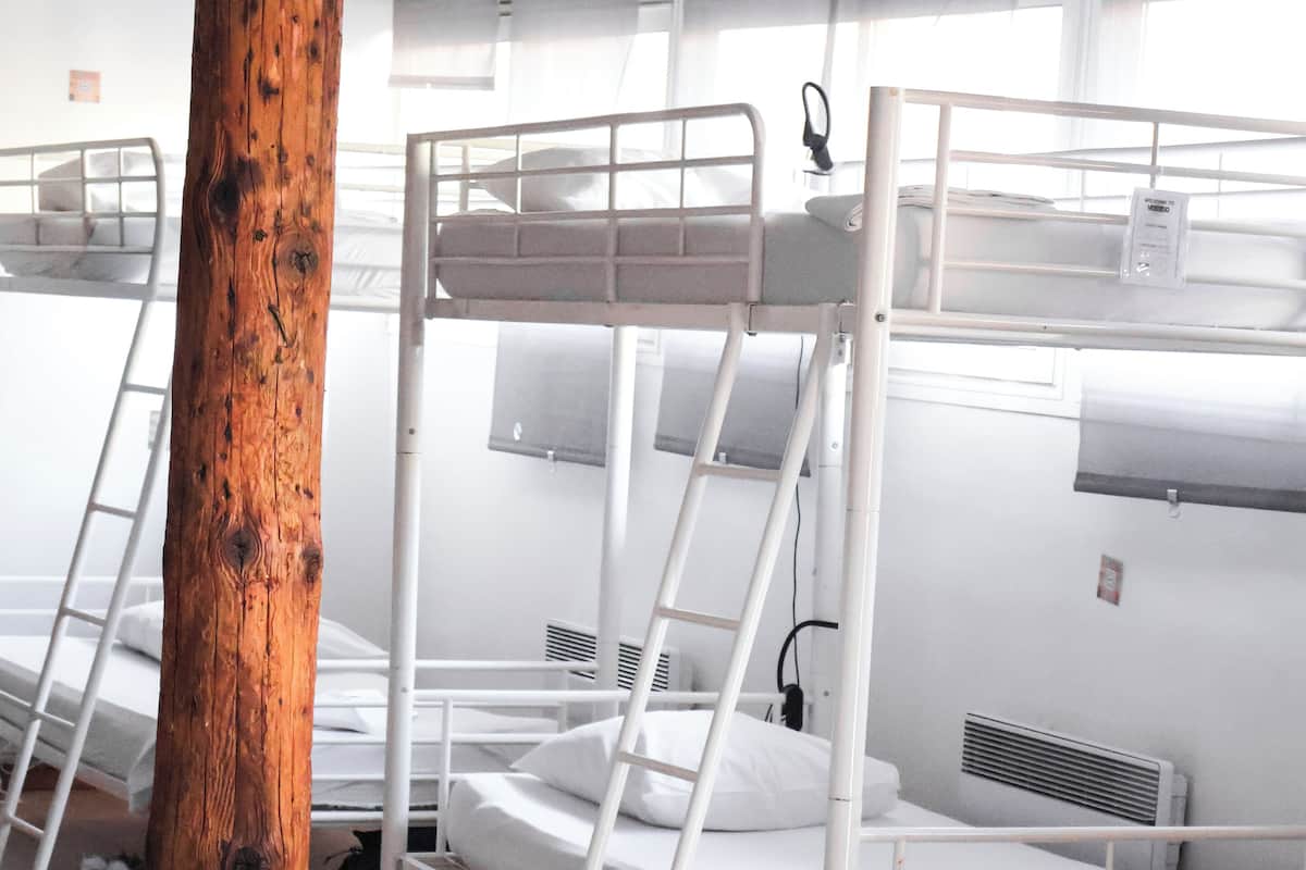 Une chambre de dortoir avec des lits superposés, des poutres en bois et des murs blancs.