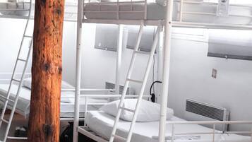Een slaapzaal met stapelbedden, houten balken en witte muren.