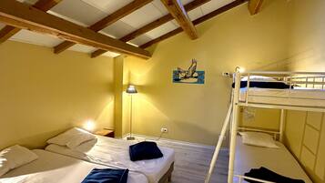 Quarto com duas camas, incluindo uma cama beliche, vigas de madeira, claraboia e luminária fixada na parede.