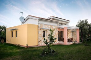 Une maison à deux étages, dotée d’une antenne parabolique, d’une façade en pierre et d’un patio couvert aménagé avec du mobilier d’extérieur.