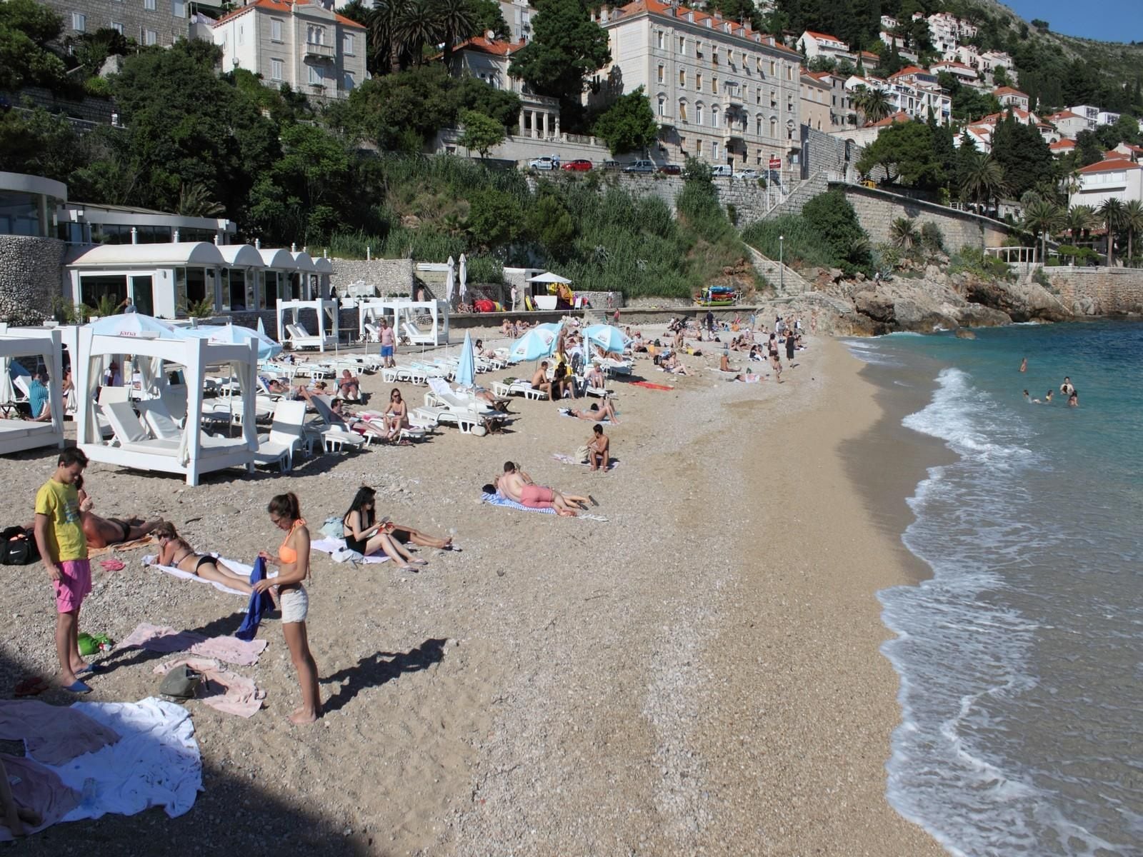 Una playa con tumbonas y sombrillas, una costa rocosa y edificios al fondo.