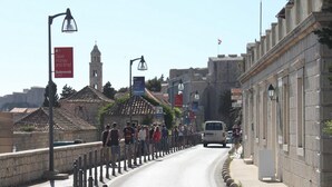 A street with a stone wall, a white van, and a crowd of people.