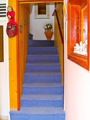 Una escalera con alfombra azul que lleva a una zona de descanso con una planta en maceta y una pequeña estatua.