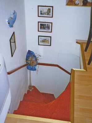A staircase with a wooden handrail and red carpet, leading to a landing with three framed pictures on the wall.