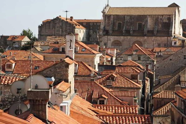 Un paisaje urbano con tejados de tejas color terracota, una iglesia destacada con un campanario, y una combinación de edificios residenciales y comerciales.