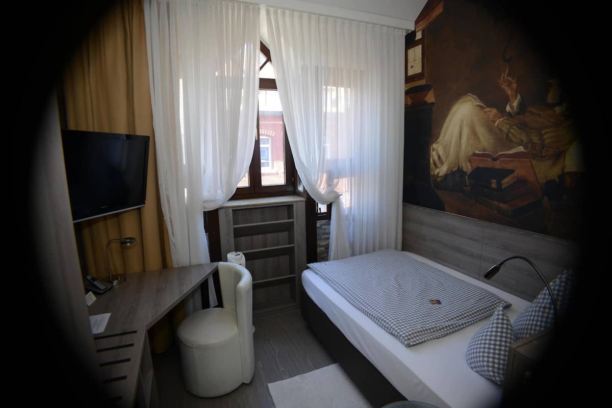 A bedroom with a bed, a desk, a chair, a TV, and a window with curtains.