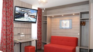 A modern hotel room with a flat-screen TV, a red sofa, a desk, and a wardrobe. - Granus (Aachen)