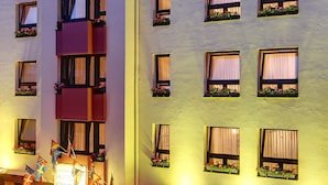 A hotel facade with multiple windows, some with curtains, and balconies with plants. - Granus (Aachen)