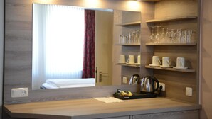 A hotel room with a wooden vanity, a mirror, a bed with white linens, a red curtain, and shelves with glasses and cups. - Granus (Aachen)