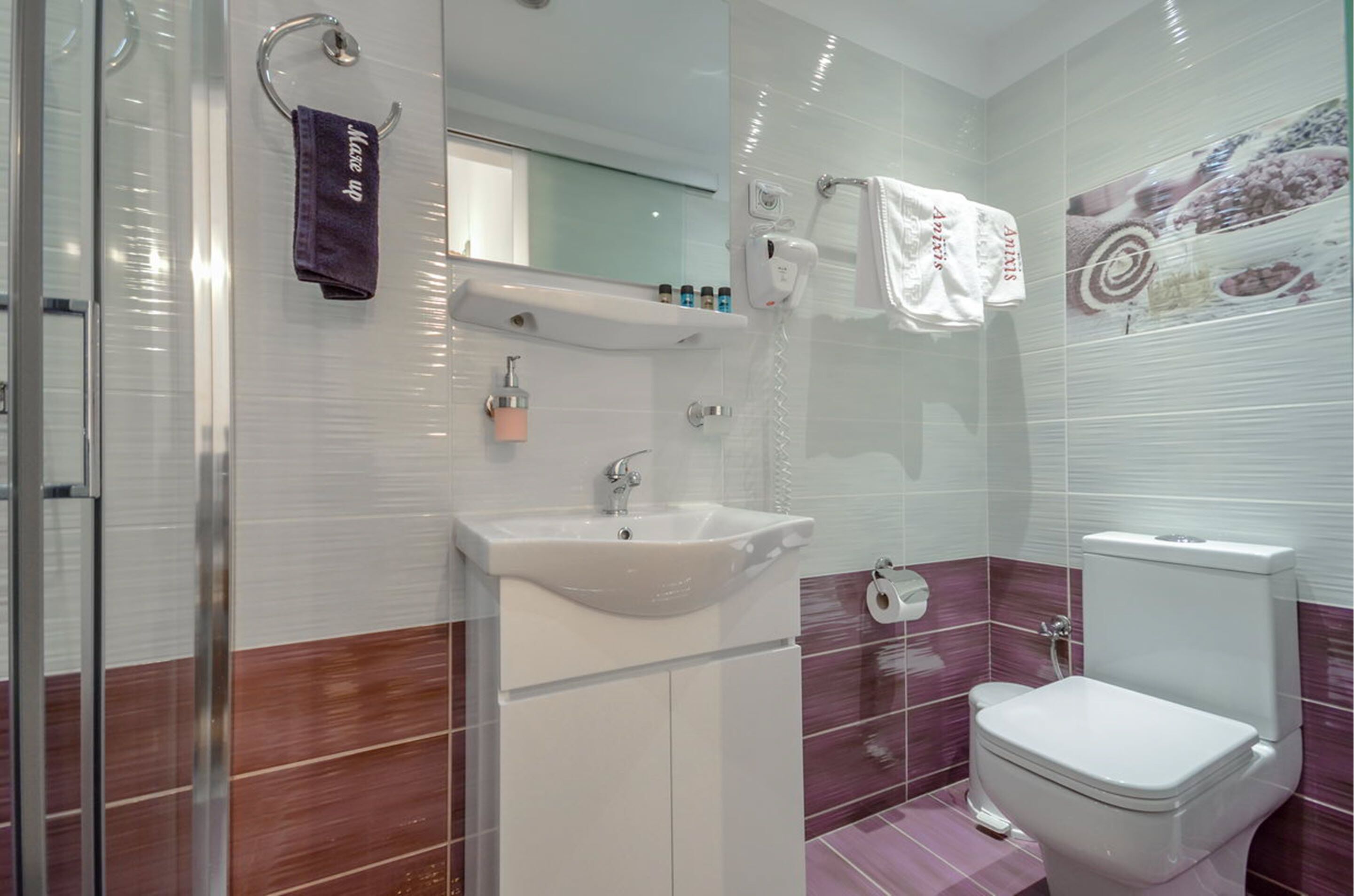 A modern bathroom with a white sink, mirror, and toilet. There are towels hanging on a rack and a glass shower enclosure.