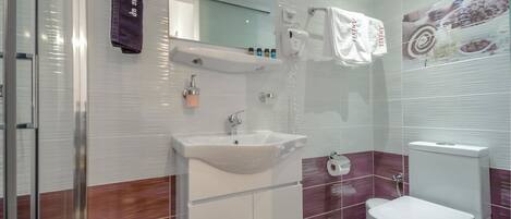A modern bathroom with a white sink, mirror, and toilet. There are towels hanging on a rack and a glass shower enclosure.