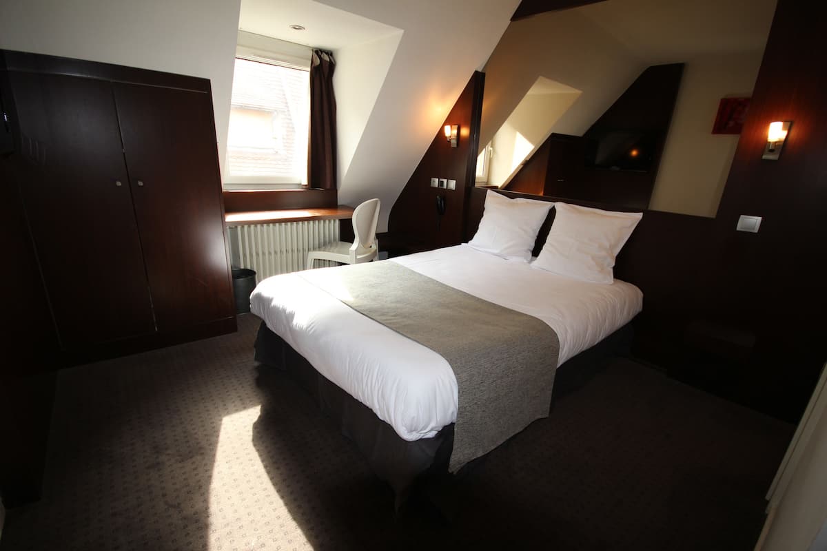 A bedroom with a large bed, a chair, a wardrobe, and a window with curtains.