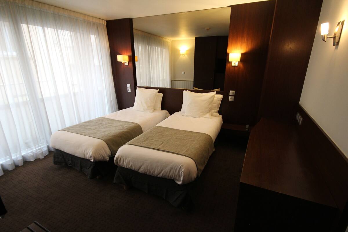 A hotel room with two beds, a large mirror, and wall-mounted lights.