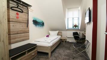 Una habitación de hotel compacta con cama, escritorio, silla, televisión y ventana.