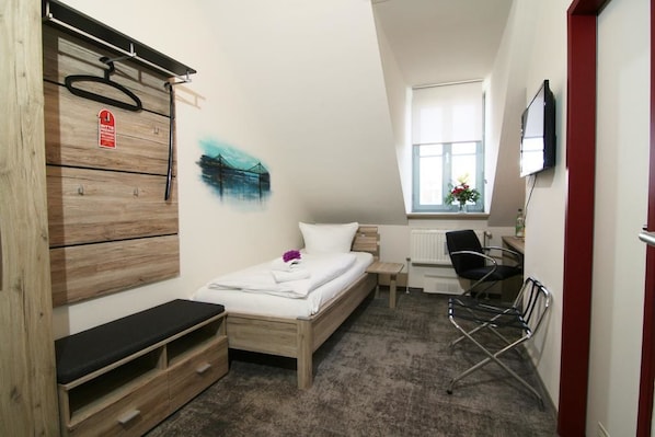 Una habitación de hotel compacta con cama, escritorio, silla, televisión y ventana.