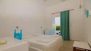 A room with two beds, a small table, and a view of the sea through a window. - Ios Plage (Ios)