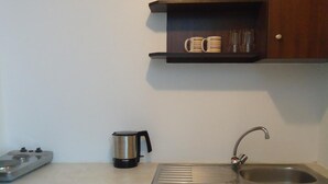 Uma cozinha compacta com máquina de lavar louça embutida, cafeteira, chaleira e pia com torneira.