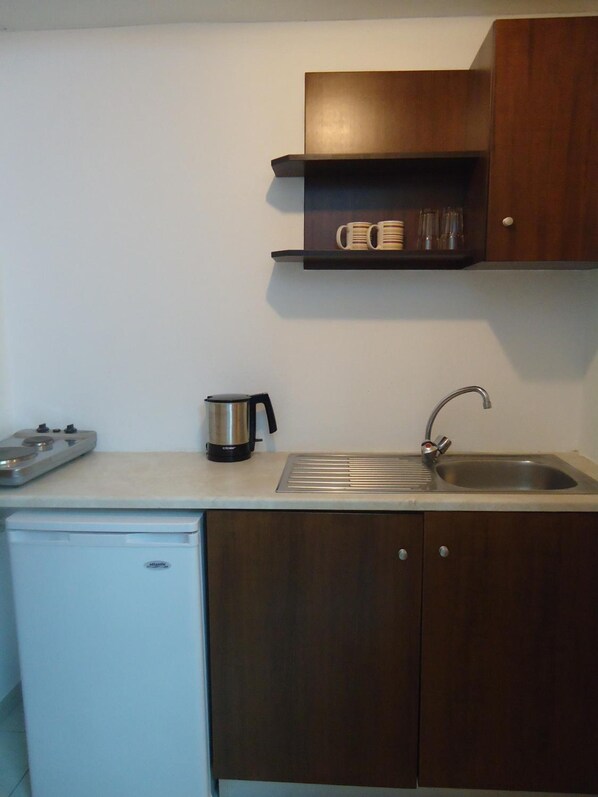 A compact kitchen with a built-in dishwasher, a coffee maker, a kettle, and a sink with a faucet.