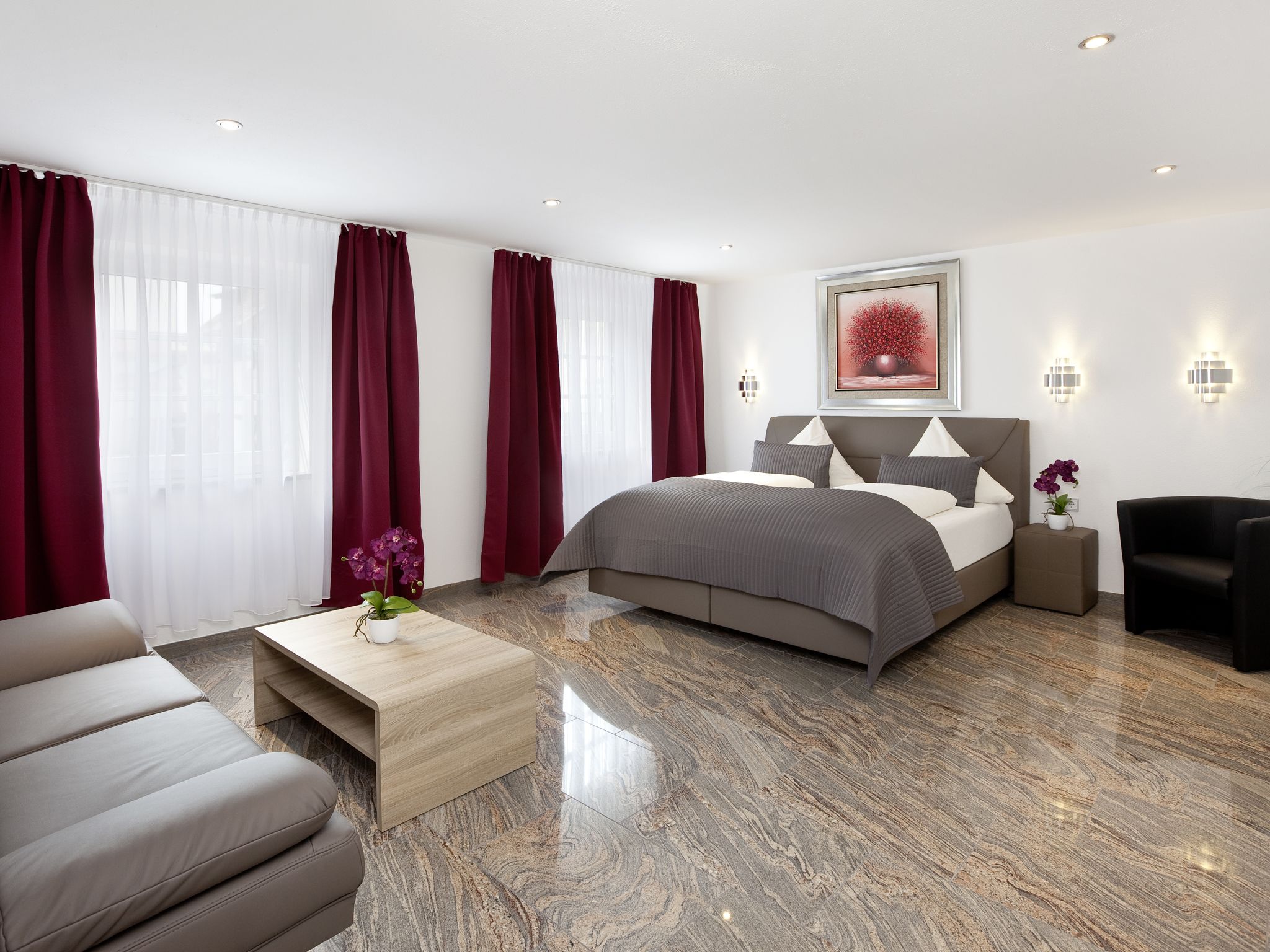 Ein modernes Hotelzimmer mit einem großen Bett, einem Holztisch, einer Couch und einem Nachttisch mit Lampe.