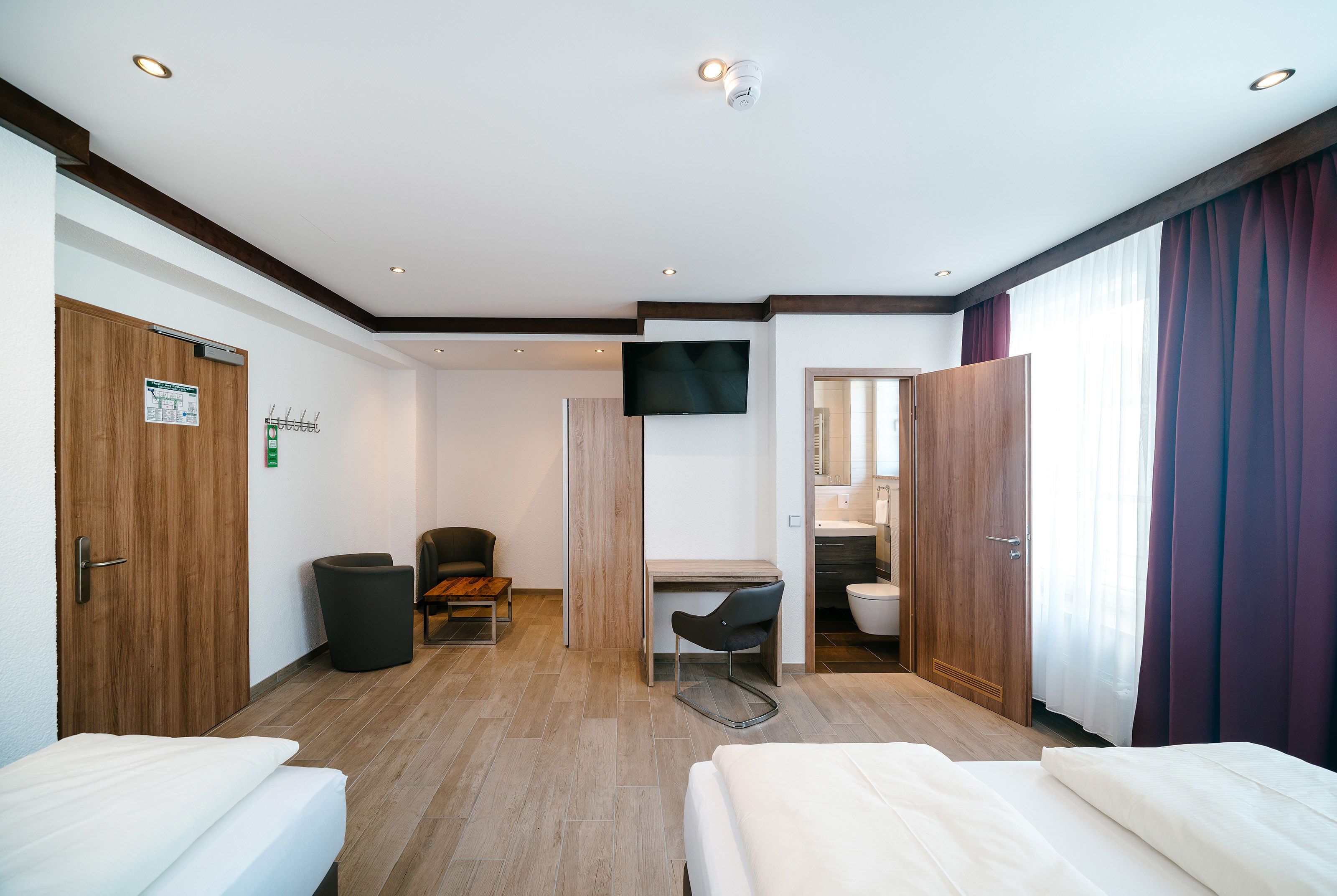 A hotel room with two beds, a desk, a chair, a TV, and a bathroom.