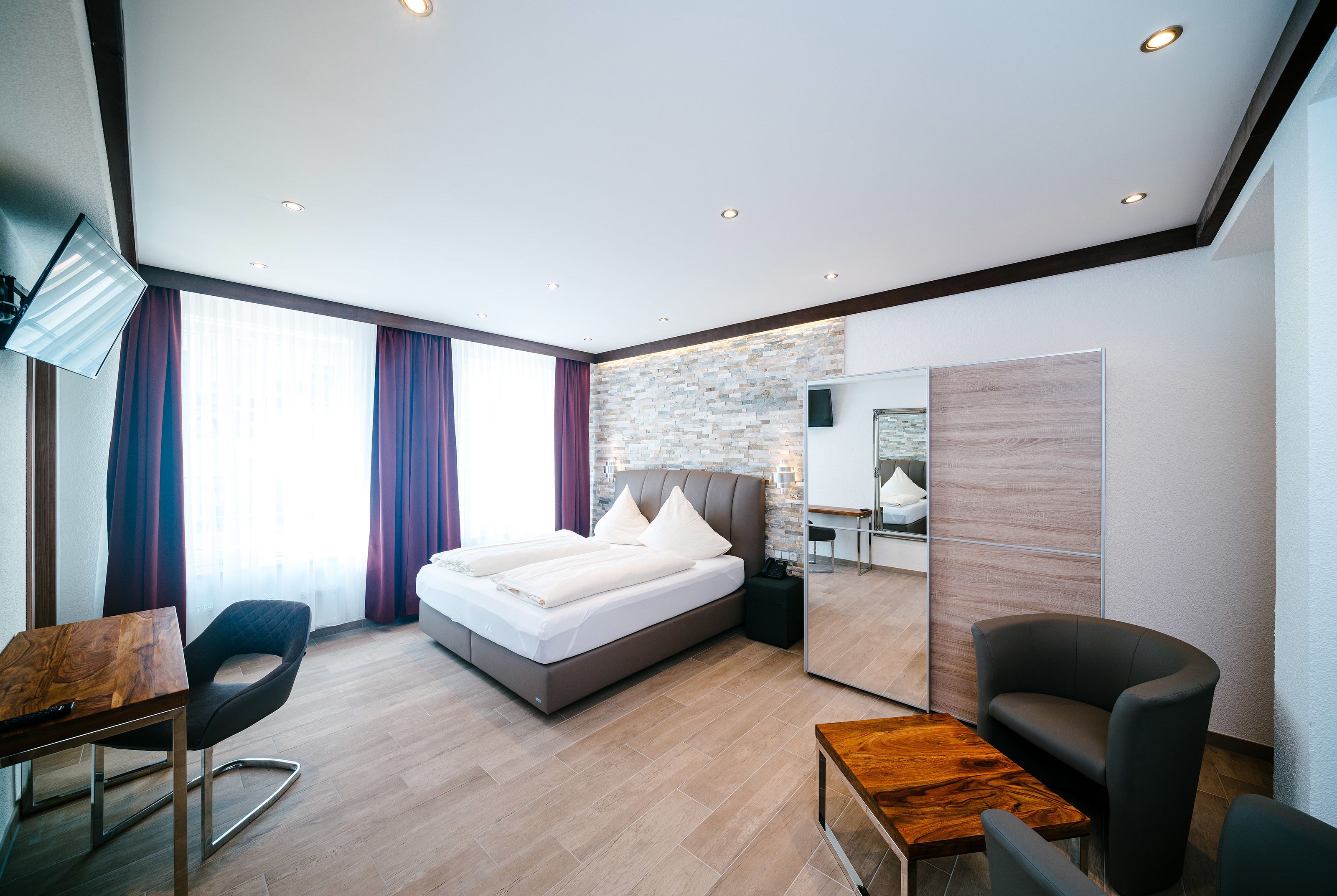 Quarto de hotel moderno com cama, escrivaninha, cadeira e uma pequena mesa.