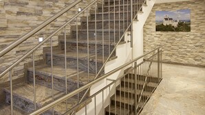 Una escalera de piedra de varios niveles con barandillas metálicas, que conduce a un rellano con un cuadro enmarco de un castillo.