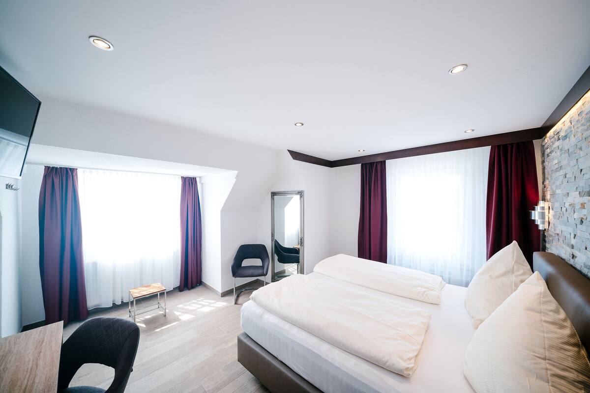A modern hotel room with a large bed, a desk, and a chair.