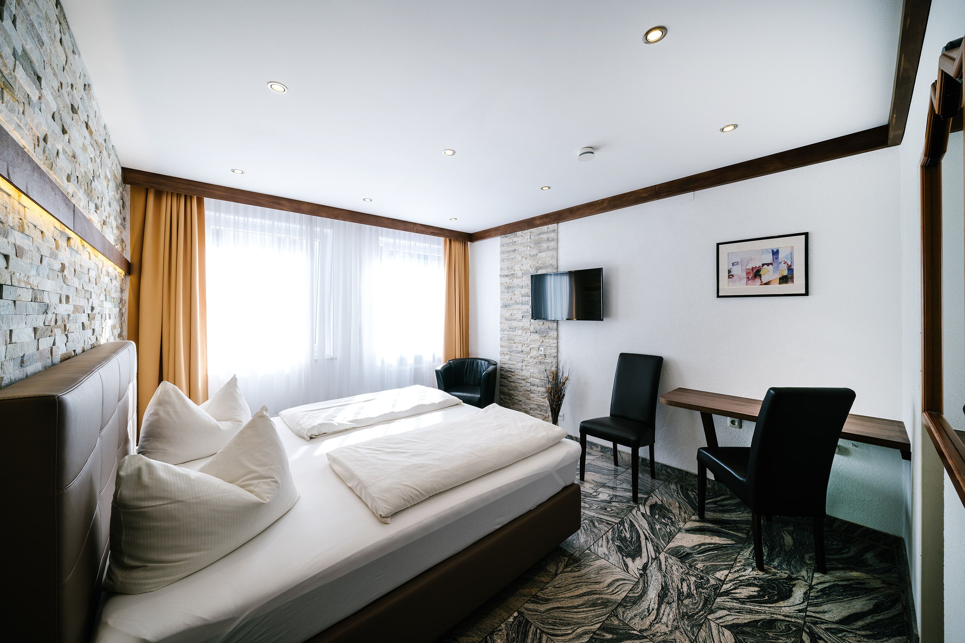 A hotel room with a bed, a desk, a chair, and a television.