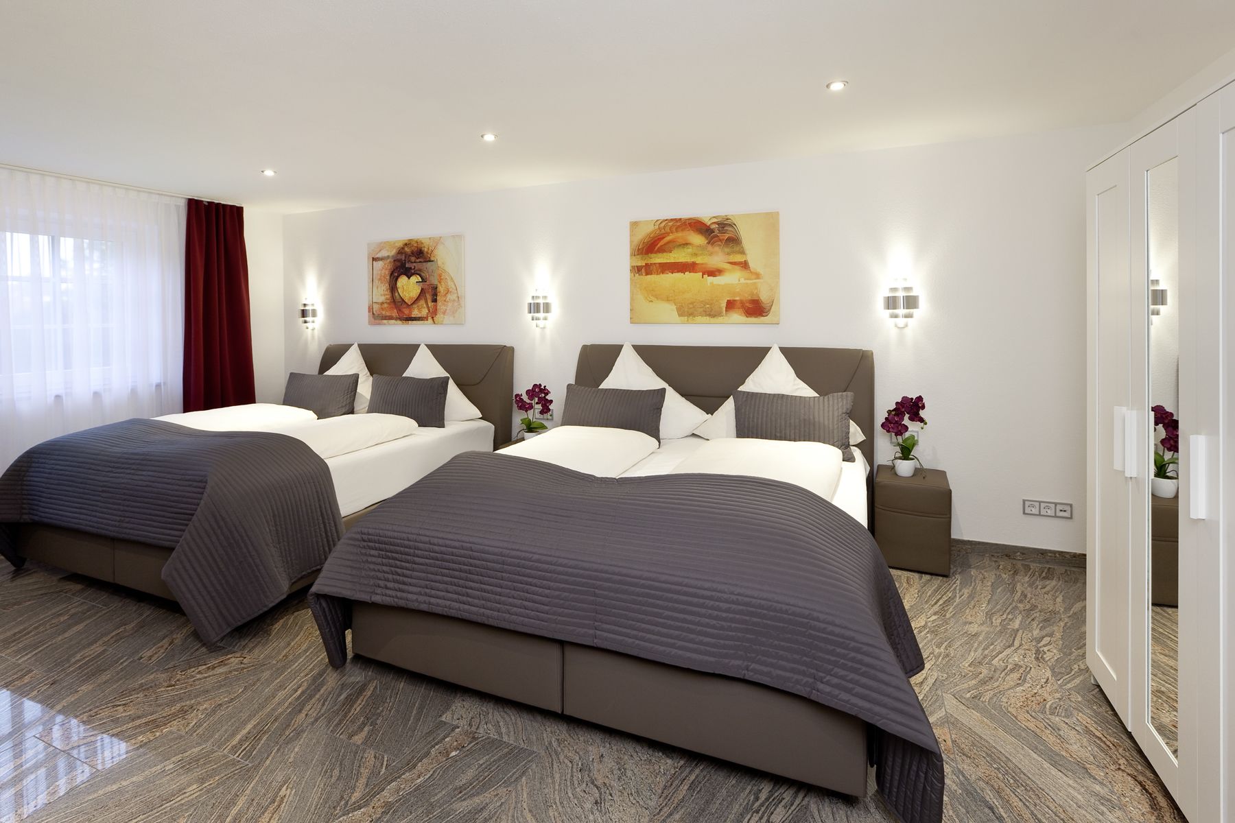 Una habitación de hotel moderna con dos camas, un ventanal con cortinas translúcidas y obras de arte en las paredes.