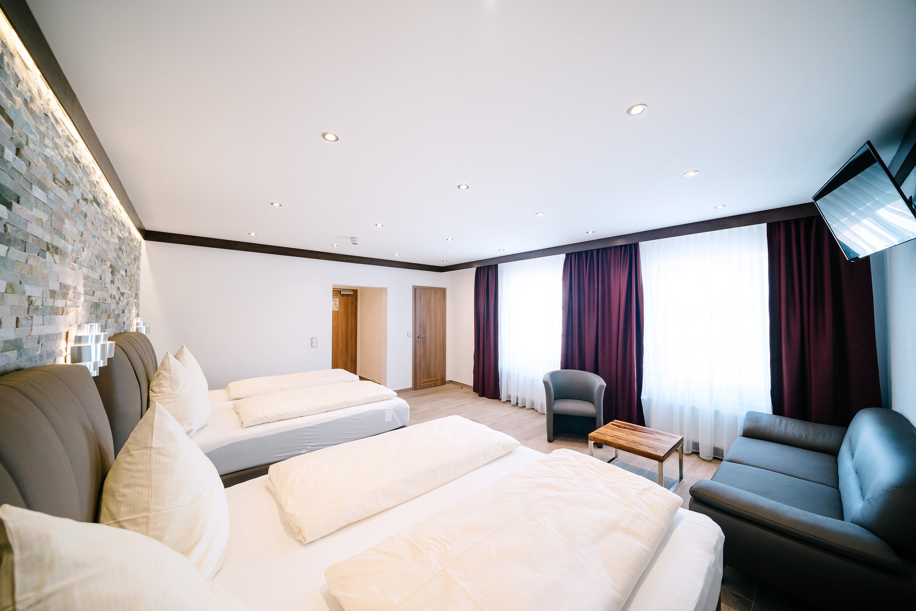 Habitación de hotel con dos camas, un sofá, una mesita y un televisor.