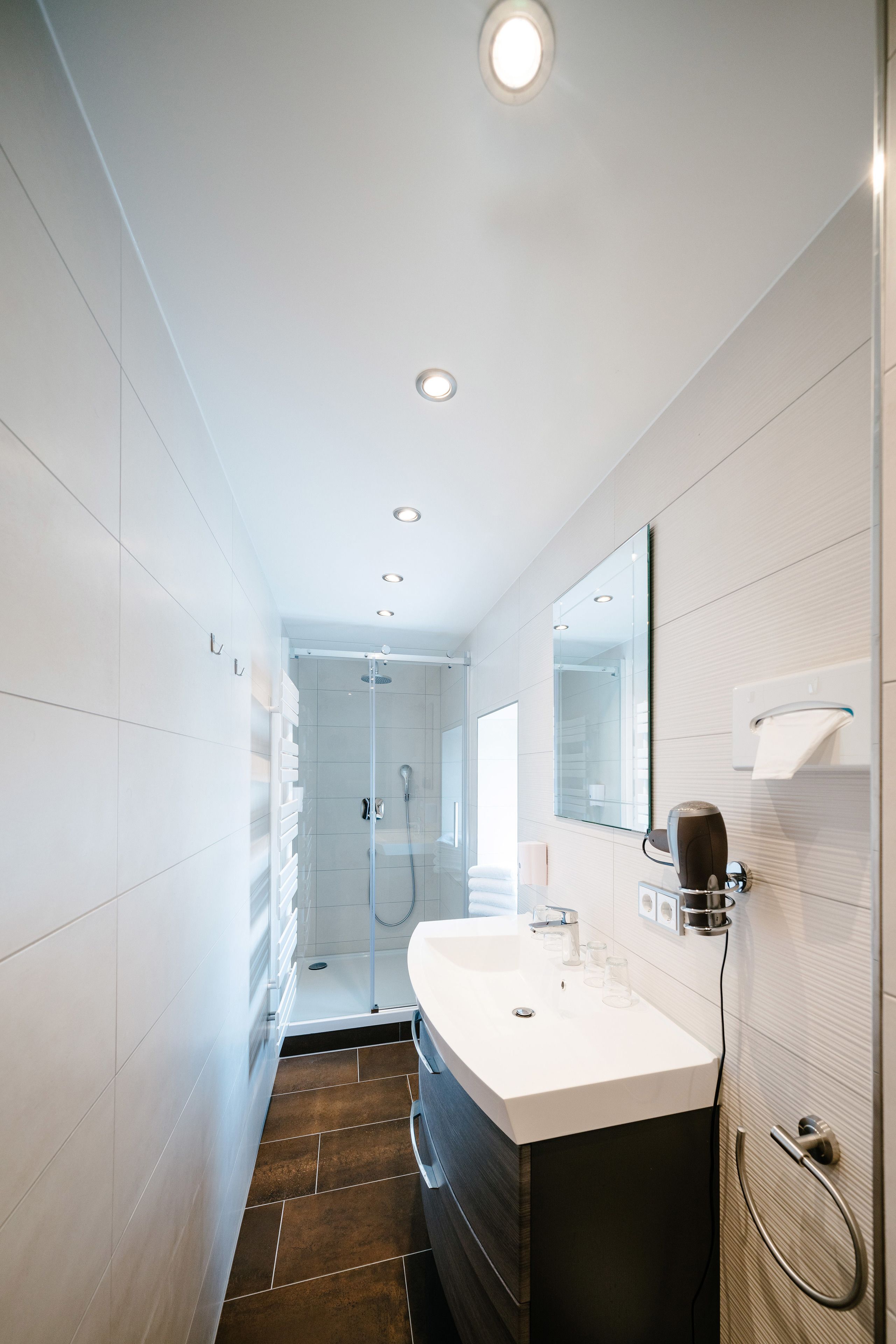 A modern bathroom with a large mirror, white sink, and shower area.