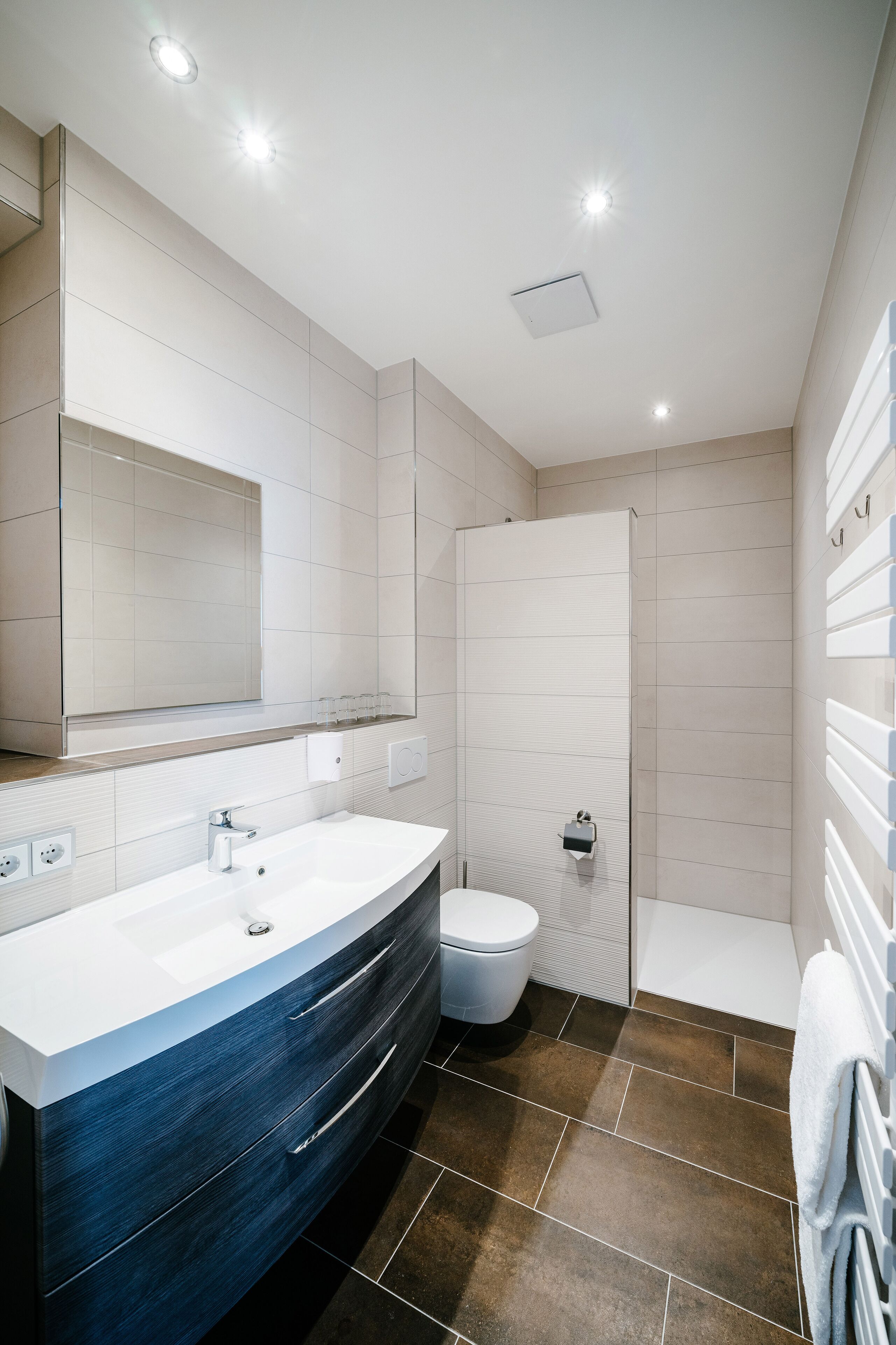 A modern bathroom with a large mirror, a white sink, a toilet, and a shower.