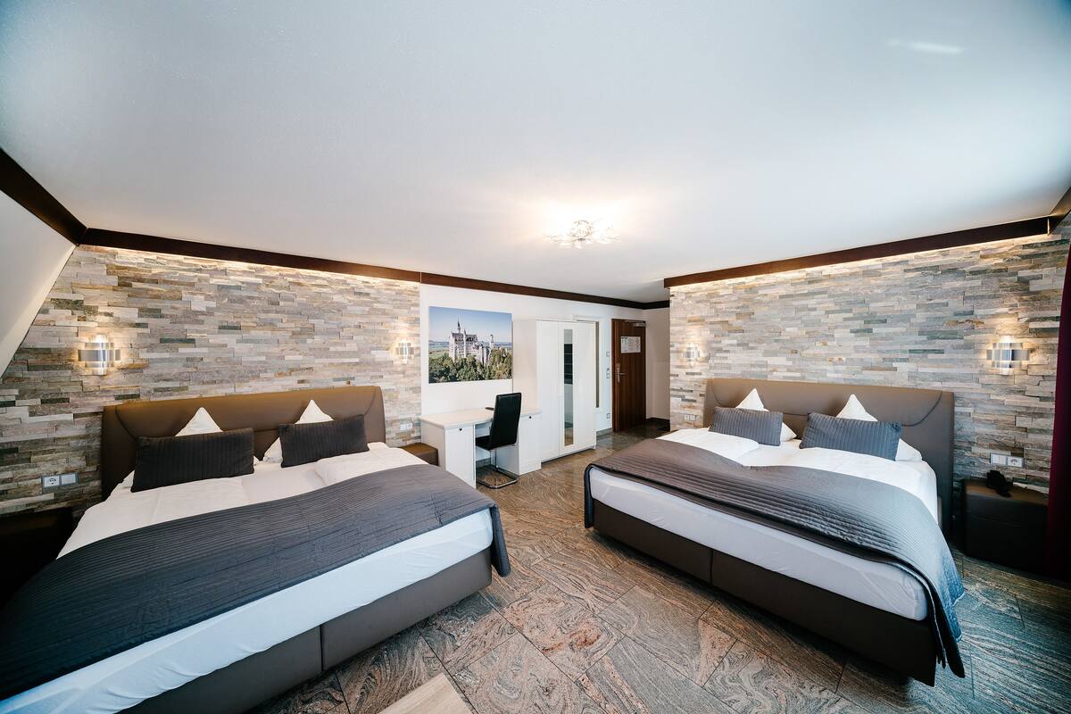 A modern hotel room with two beds, a desk, and a stone wall.