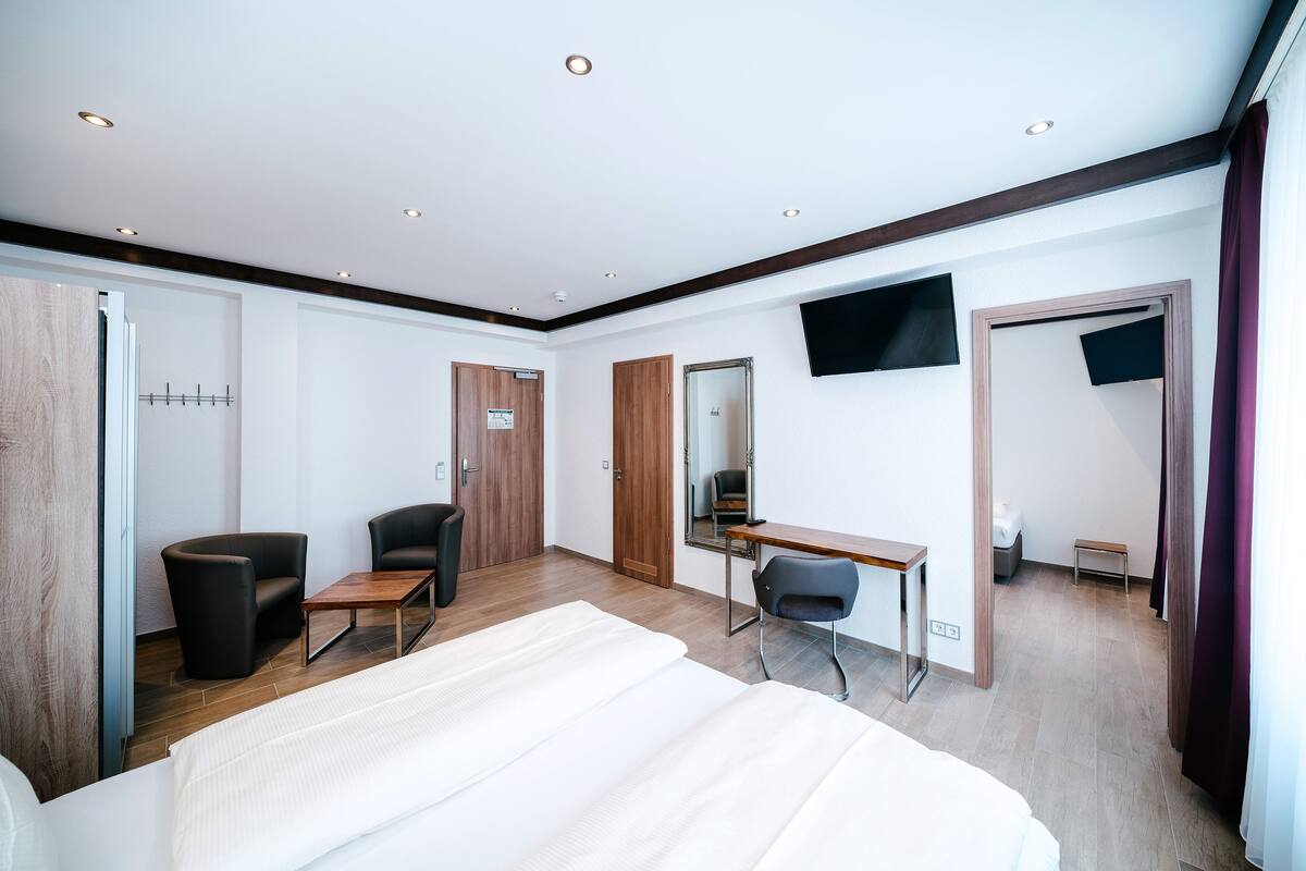 A hotel room with a bed, two chairs, a desk, and a TV.