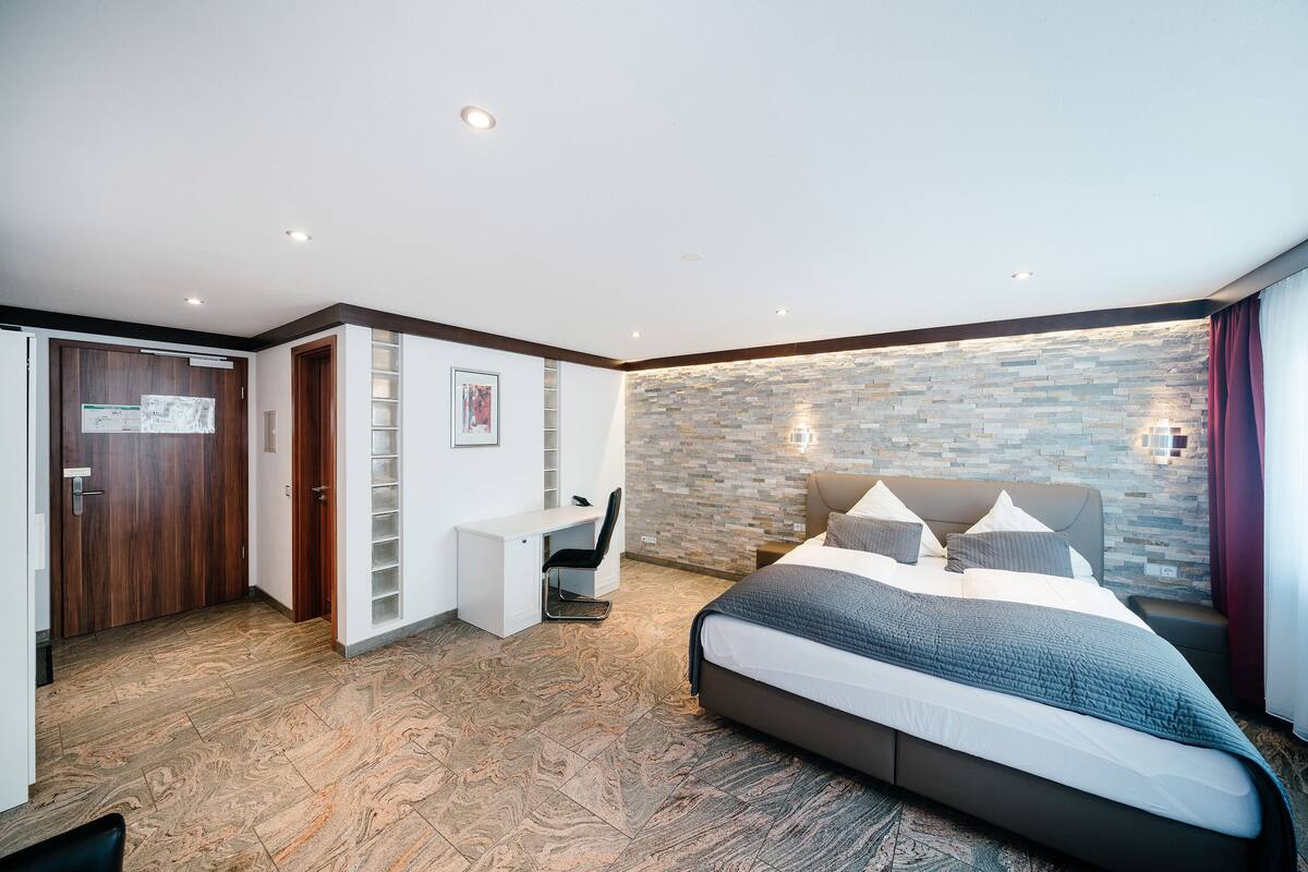 A bedroom with a bed, a desk, and a stone wall.