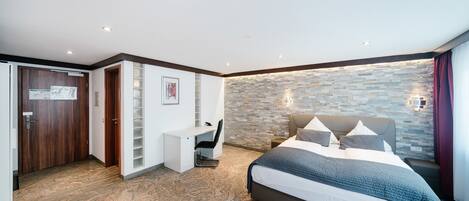 Une chambre à coucher avec un lit, un bureau et un mur en pierre.