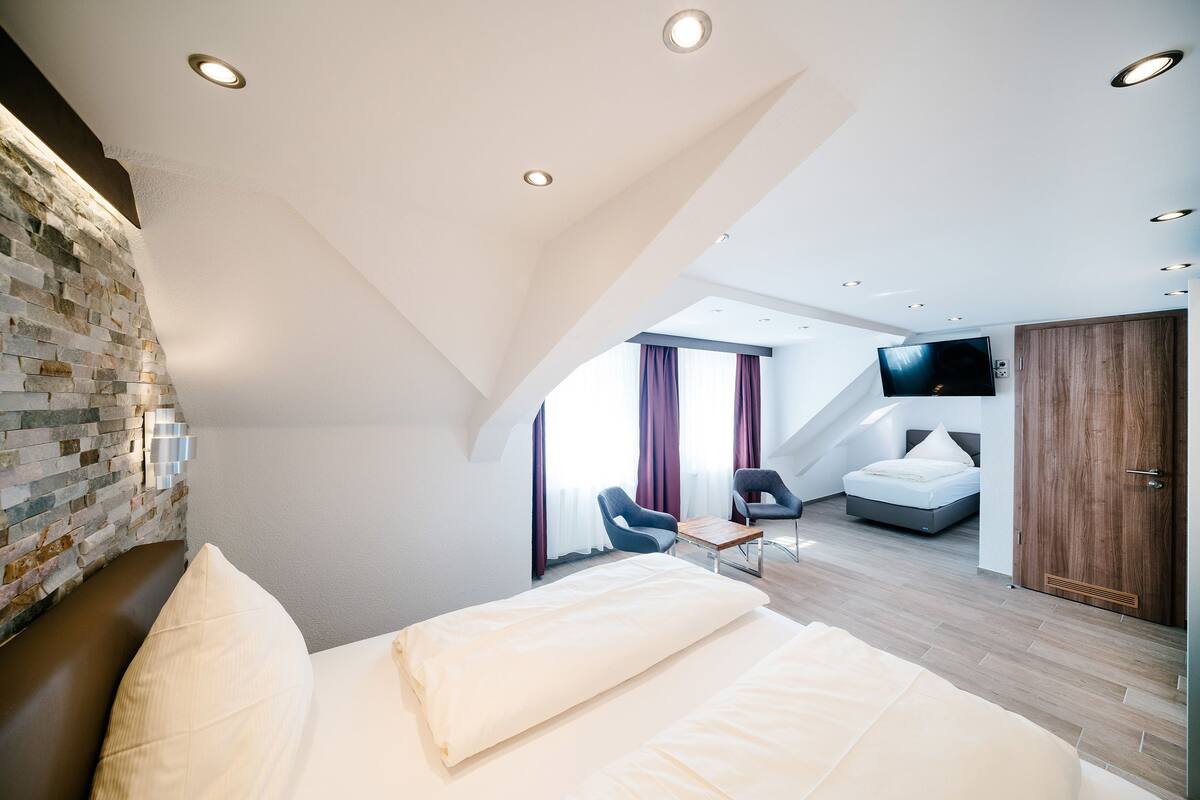 A modern hotel room with a loft bed, a stone accent wall, a flat-screen TV, and a view of the city.