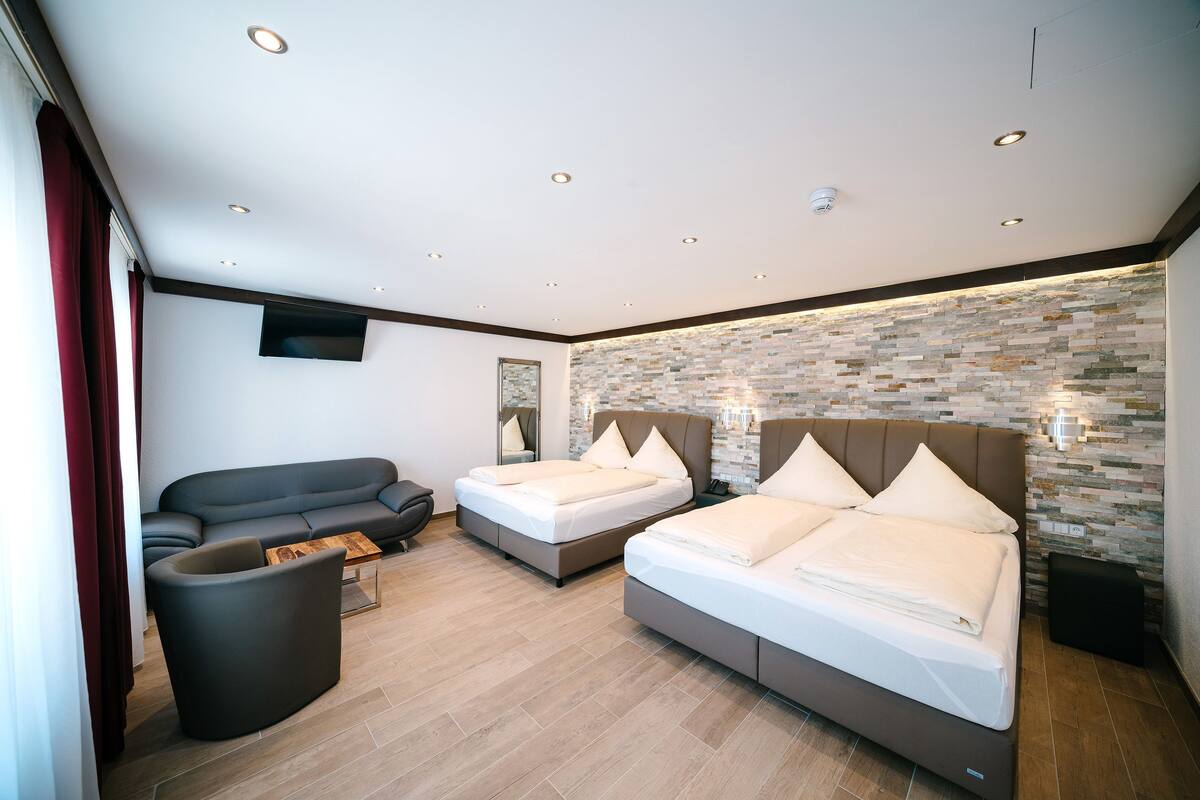 A modern hotel room with two beds, a sofa, a coffee table, and a stone-patterned wall.