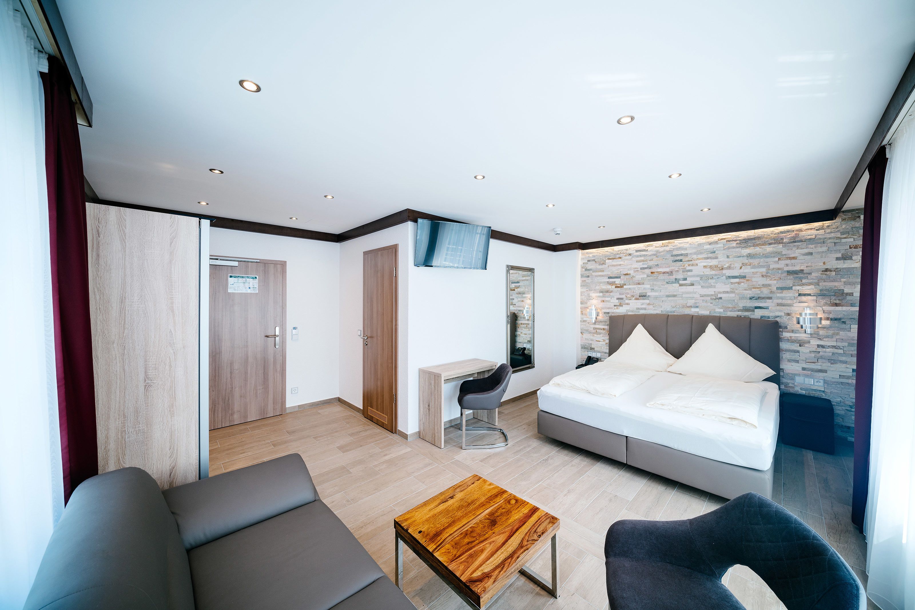Una habitación de hotel moderna con cama, escritorio, sofá y una pequeña mesa de madera.
