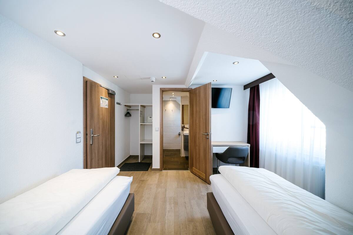 A hotel room with two beds, a desk, a TV, and a bathroom visible through an open door.
