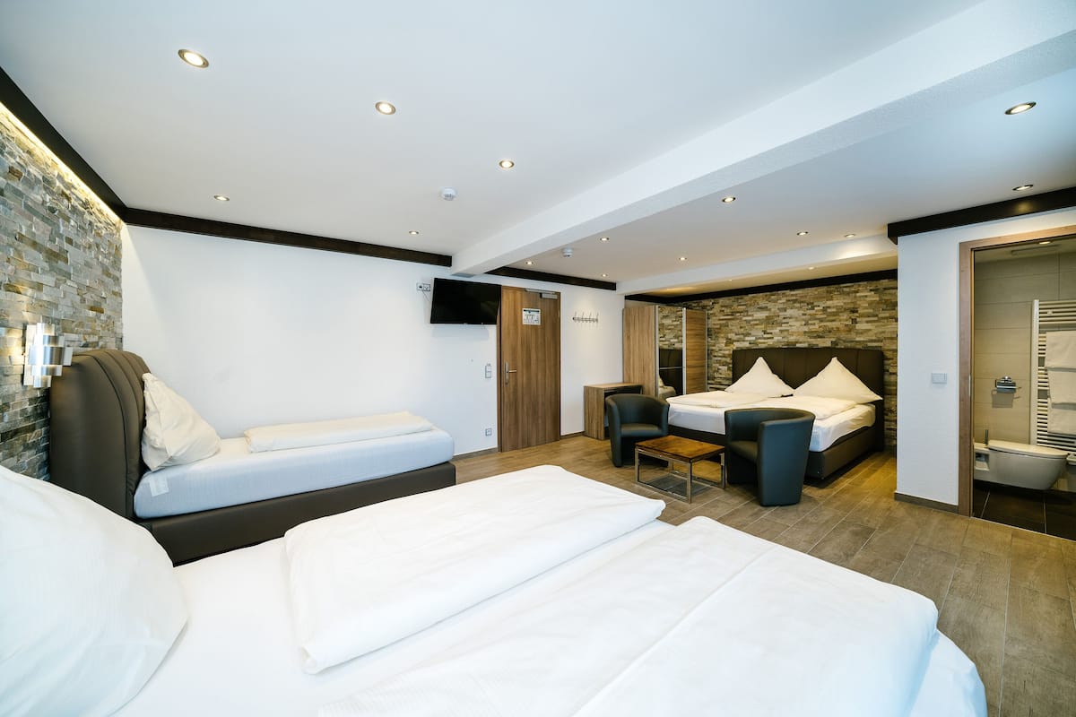 A modern hotel room with two single beds, a small desk, and a shower area.