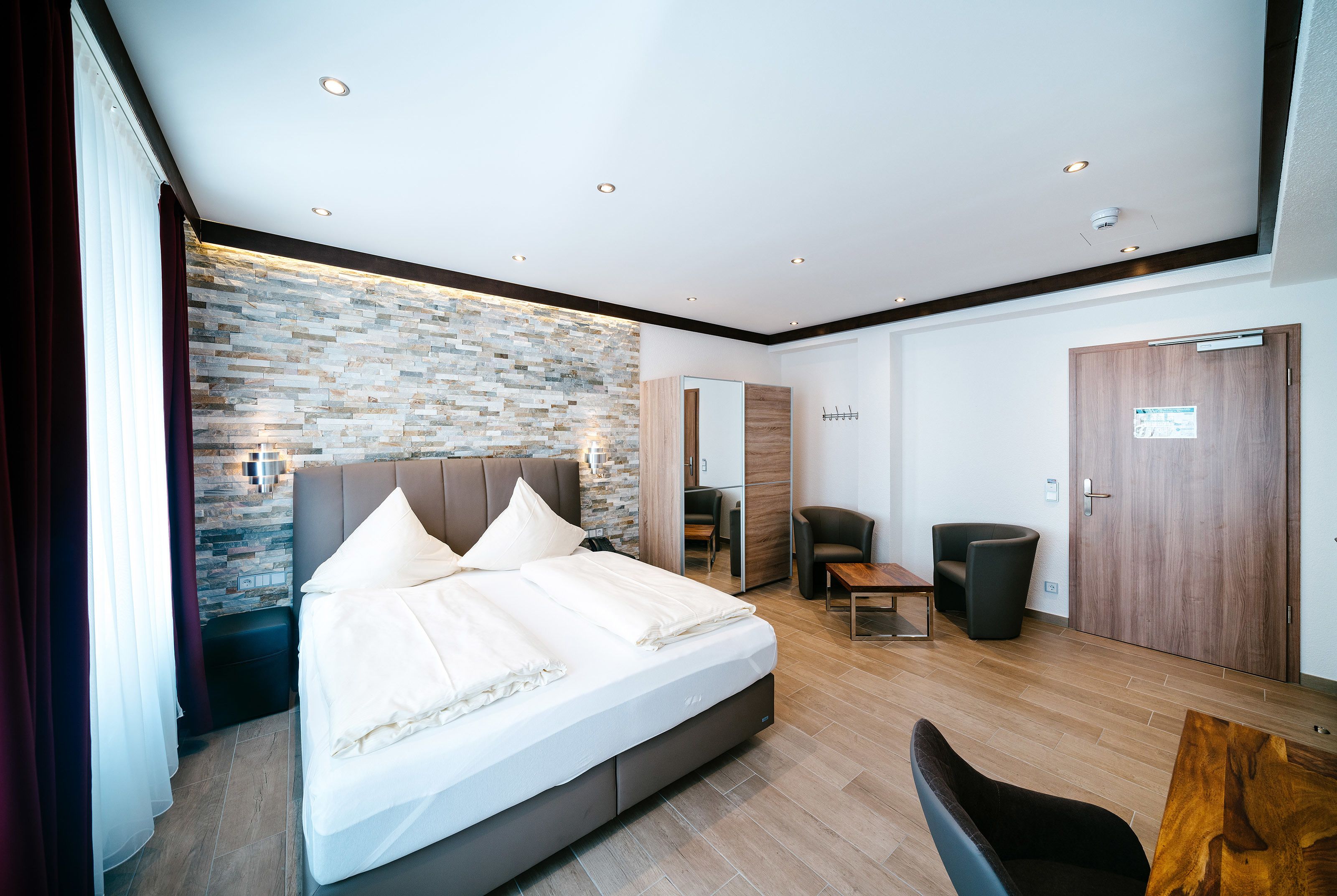 Une chambre d’hôtel moderne dotée d’un grand lit, d’un coin salon et d’un mur décoratif en pierre.